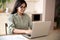 Smiling indian young woman typing on laptop computer working at home office.