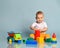 Smiling infant baby boy toddler in yellow pants is sitting surrounded by toys, is busy with big red cylinder, playing