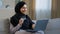 Smiling islamic girl customer in hijab sitting on sofa make online order use laptop enter credit card number for