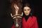 Smiling jockey woman standing with brown horse in stable, black background