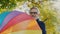 A smiling, joyful, bearded, grey-haired man with glasses on, spinning a vivid rainbow umbrella in the middle of the park