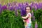 Smiling kid girl holding a large bouquet of purple lupins in a flowering field