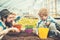 Smiling kid playing with daddy in greenhouse. Bearded man in blue vest, yellow shirt and hat looking at his son, mommy