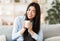 Smiling korean woman drinking coffee while resting on couch at home