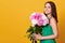 Smiling lady in green dress looking directly at camera with charming smile, holding peony flowers, has present from husband,