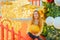 Smiling lady holding a huge Christmas ball while sitting near a festive fir tree and a sparkling decorative train