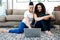 Smiling lesbian couple sitting on rug and using laptop