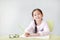 Smiling little Asian child girl write in a book or notebook with pencil sitting on kid chair and table against white background