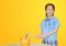 Smiling little asian girl in school uniform preparing to break the piggy bank with a hammer on yellow background at table.