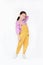 Smiling little Asian kid girl in pink-yellow dungarees poses touched hair keep back isolated on white background. Full length of