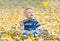 Smiling little baby boy playing with yellow leaves in the park. Autumn. Funny cute child making vacations and enjoying Autumn. Hap