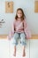 Smiling little barefoot girl in oversized sweater sitting on a shelf at home