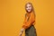 Smiling little blonde kid girl 12-13 years old in turtleneck, jumpsuit isolated on orange yellow background children