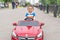 Smiling little boy driving by toy car. Active leisure and sports for kids. Portrait of happy little kid on the street. Funny cute