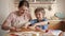 Smiling little boy helping mother rolling pizza dough on wooden cutting board. Children cooking with parents, little