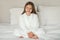 Smiling little caucasian girl in bathrobe after shower sit on white soft bed, enjoy spare time and beauty care