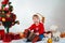 Smiling little child in a Christmas costume with an accordion in his hands sitting under the Christmas tree