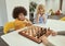 Smiling little diverse boys sitting together at the table and playing chess in school