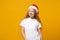 Smiling little ginger kid Santa girl 12-13 years old in white t-shirt, Christmas hat isolated on yellow background