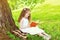 Smiling little girl child reading a book on the grass near tree