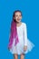 Smiling little girl with long pink hair, dressed in ballet white dress, on a blue background. Verical view.