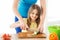 Smiling little girl with mother chopping cucumber