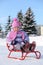 Smiling little girl in pink scarf and hat sits on sled
