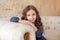 Smiling little girl sitting on a couch in living room. Inspired little girl with big eyes and curly hair. Beautiful young girl res