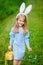 Smiling little girl wearing bunny ears nd holding wicker basket with yellow eggs