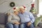 Smiling loving elderly couple in Christmas festive caps sitting on sofa and hugging during Christmas