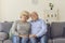Smiling loving elderly couple wife and husband in jeans sitting on sofa and hugging