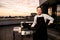 Smiling male chef holds tongs in his hand and standing near barbecue equipment.