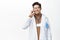 Smiling male doctor answer phone call, talking on cellphone, wearing clinic uniform robe, standing over white background