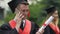 Smiling male graduating student holding university diploma, talking on phone