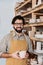 smiling male potter holding cup and standing at shelves with ceramic