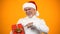 Smiling male retiree in santa claus hat pointing finger at red giftbox, discount