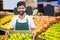 Smiling male staff holding a basket of green apple at supermarket