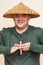 Smiling man with Asian straw hat showing strange hand sign.