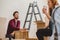 Smiling man assembling a cabinet and his girlfriend drinking coffee while furnishing interior