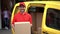 Smiling man from delivery hols cardbox and stands near yellow car