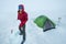 Smiling man dressed red warm mountaineering down jacket making the protective wall from snow bricks around camp tent on glacier