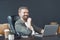 Smiling man finds joy in work as he diligently operates laptop on well-organized desk within bustling office environment