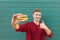 Smiling man holds an appetizing burger in his hands and shows a thumbs up. Fast food