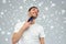 Smiling man shaving beard with trimmer over snow