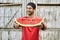 Smiling man with stubble holds slice of watermelon on wooden fence background