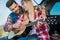 smiling man teaching smiling girlfriend to play on acoustic guitar on car