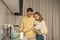 Smiling man and woman, couple in yellow hoodies washing the dishes, woman holding white dog