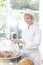 Smiling mature chef arranging fresh sweet food in container at restaurant counter