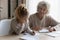 Smiling mature grandmother helping little granddaughter with school homework