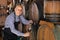 Smiling mature man seller filling wine from wood